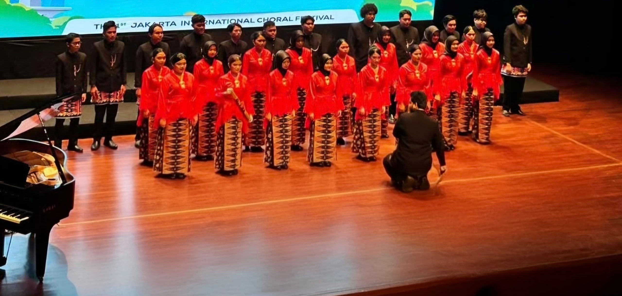Penampilan Jakarta Serenade Choir (JSC) Pendidikan Musik UNJ dengan kostum merah-hitam di atas panggung Teater Besar Taman Ismail Marzuki saat berkompetisi di ajang The 1st Jakarta International Choral Festival 2025.